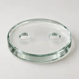Centered studio photograph of a round translucent glass food-safe fermentation weight with two finger holes on a neutral light background.