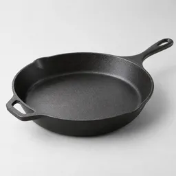 A centered dark cast-iron oven-safe skillet shown at a slight three-quarter angle on a neutral light background.