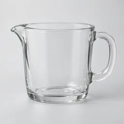 Centered clear borosilicate glass heatproof measuring cup with a pouring spout and sturdy handle on a pale neutral background.