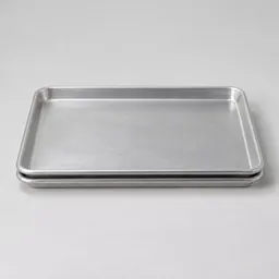 Centered studio photograph of two plain silver rimmed baking sheets stacked together on a light neutral background.