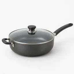 Centered studio photograph of a large deep dark gray skillet with a clear glass lid, long handle, and helper handle on a neutral light background.