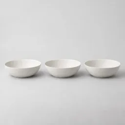 Three matching shallow white ceramic kitchen bowls centered on a light neutral background.