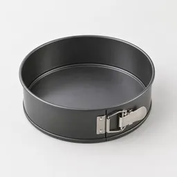 Centered unbranded springform pan with a dark metal base and side-release latch on a light neutral background.