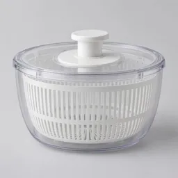 A complete salad spinner with a clear outer bowl, perforated inner basket, and fitted lid, centered on a light neutral background.