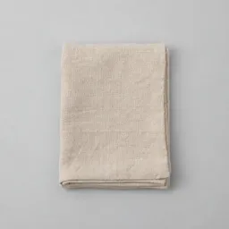 A neatly folded plain pale beige kitchen towel photographed alone on a light neutral background.