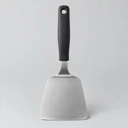 Centered wide stainless-steel kitchen turner with a broad rounded blade and dark handle on a light neutral background.