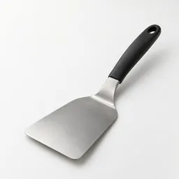 Realistic studio photograph of a plain black-handled stainless-steel kitchen spatula centered on a neutral light background.