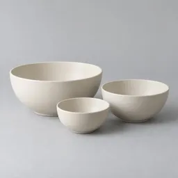 Centered studio photograph of three plain ivory ceramic serving bowls in graduated sizes on a light neutral background.