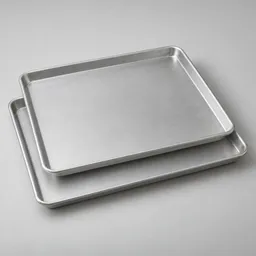 Two large unbranded rimmed aluminum baking sheets centered on a light neutral background, with one slightly offset above the other.