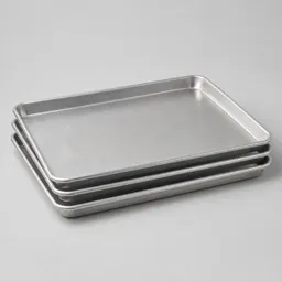 Centered stack of plain aluminum baking sheets on a neutral light background.