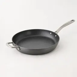 Centered 12-inch skillet with a dark cooking surface, long handle, and helper handle photographed against a neutral light background.