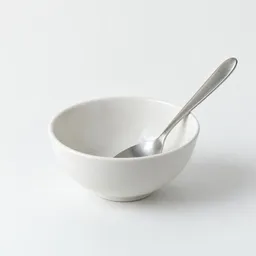 Small plain bowl with a stainless-steel spoon centered on a light neutral background.